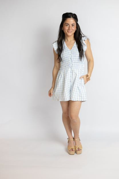 Woman wearing a light blue gingham ruffle romper on a white background