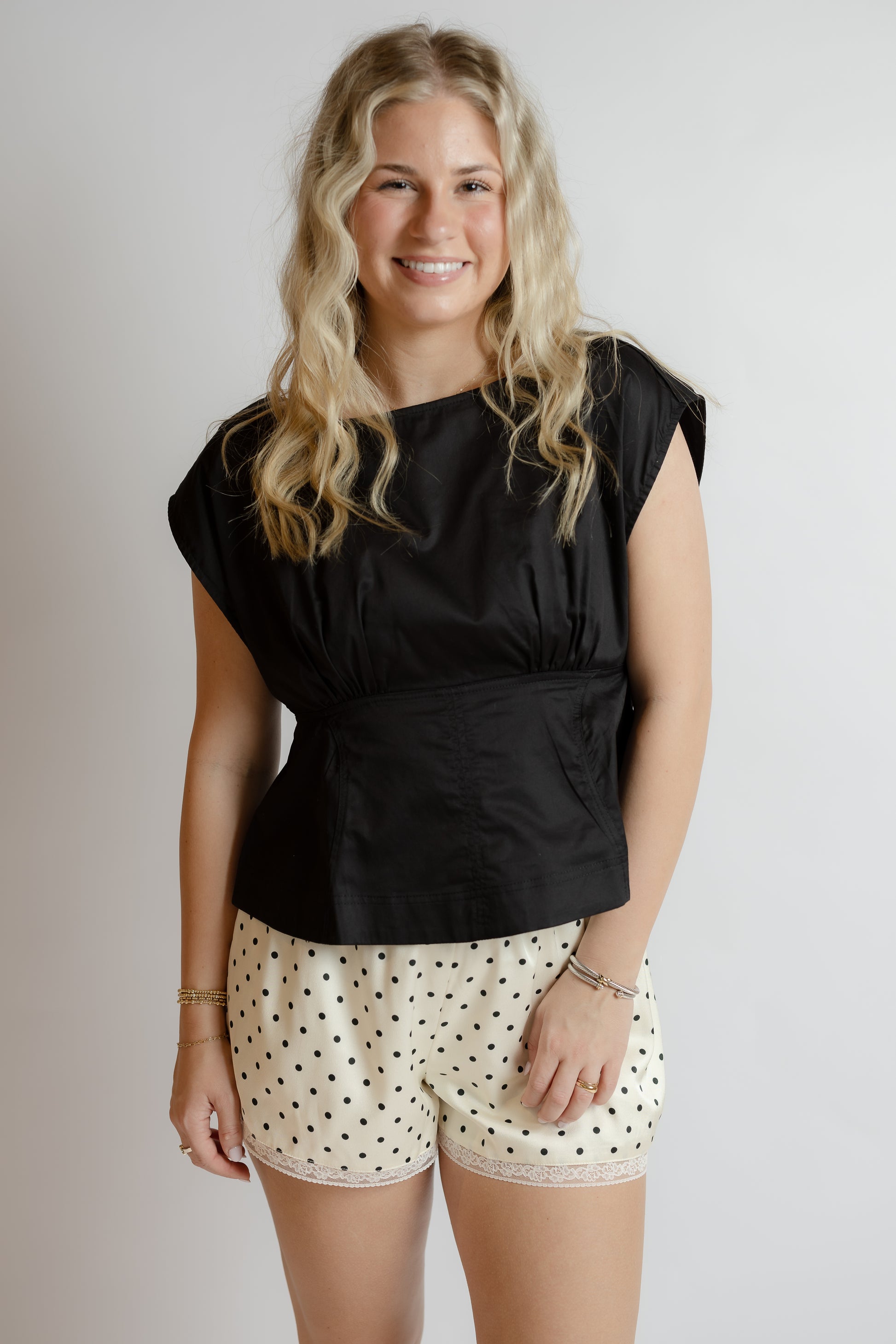 Woman wearing a black top and polka dot shorts on a plain background