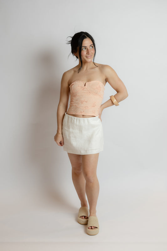 Woman wearing a strapless top and white skirt against a plain background