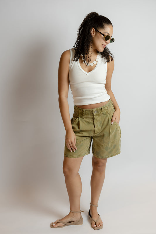 Woman wearing a white tank top and green shorts against a plain background