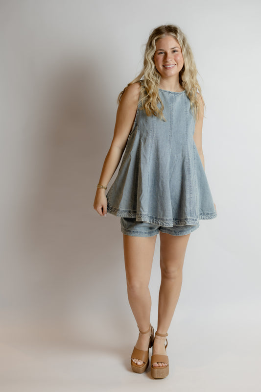 Woman wearing a light blue denim set and sandals on a plain background