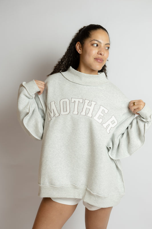 Person wearing a gray sweatshirt with 'MOTHER' printed on it against a plain background