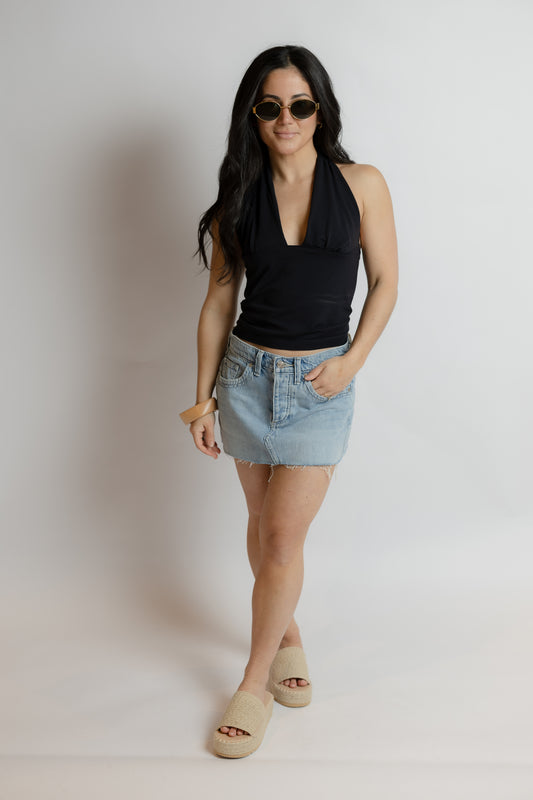 Woman wearing a black halter top and denim skirt against a plain background