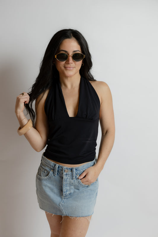 Woman wearing a black halter top and denim skirt with sunglasses on a plain background