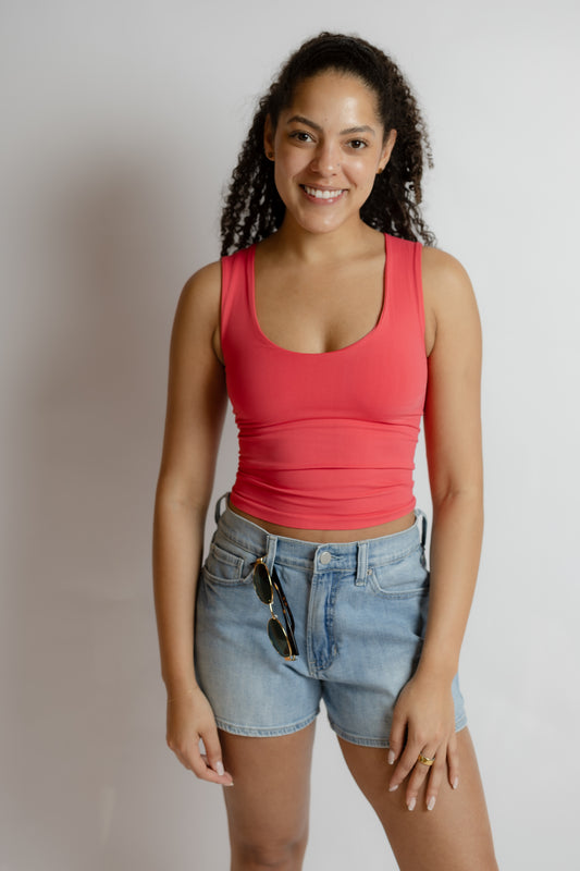 Woman wearing a red tank top and blue shorts against a plain background