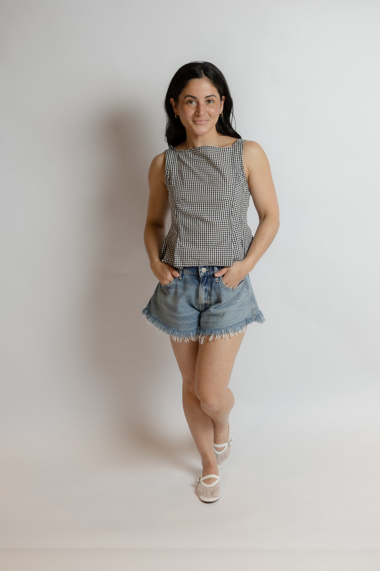 Woman wearing a checkered top and denim shorts against a plain background