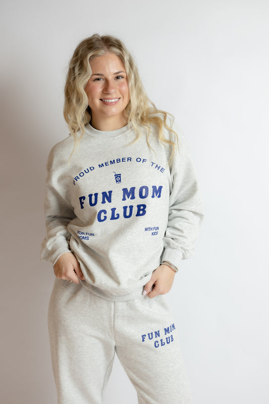 Woman wearing a 'Proud Member of the Fun Mom Club' sweatshirt and pants on a plain background