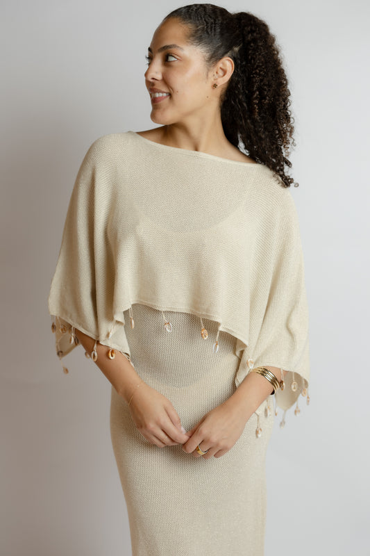 Woman wearing a beige poncho over a matching dress against a plain background