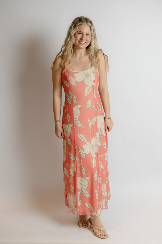 Woman wearing a coral floral dress against a plain background
