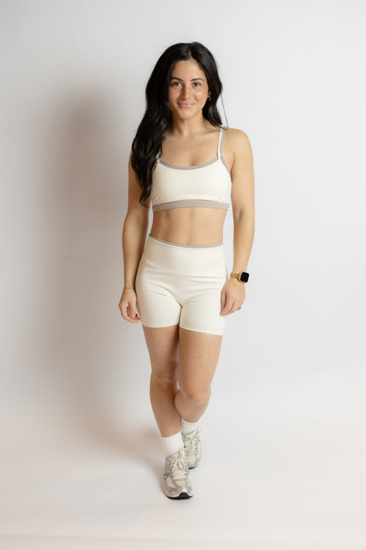 Woman wearing a white sports bra and shorts athletic set on a plain background