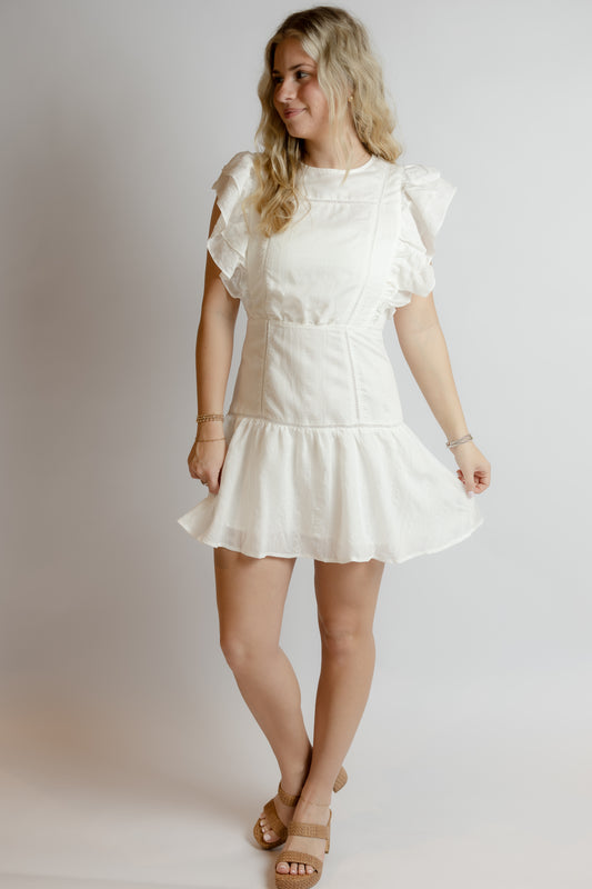 Woman wearing a white dress with ruffled sleeves against a plain background