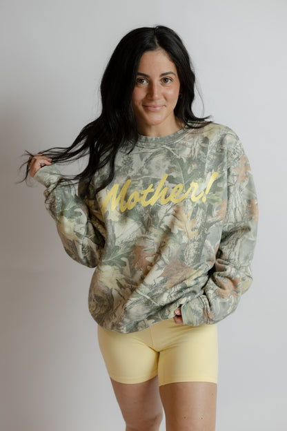 Woman wearing a camouflage sweatshirt with 'Mother!' text on a plain background
