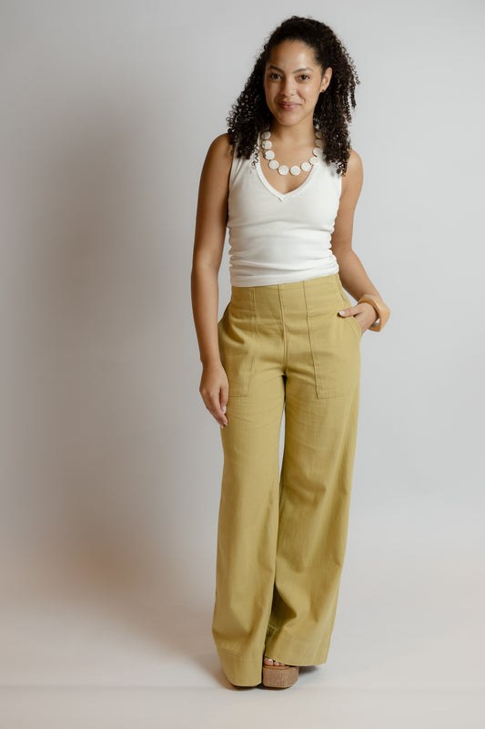 Woman wearing a white tank top and mustard yellow pants against a plain background