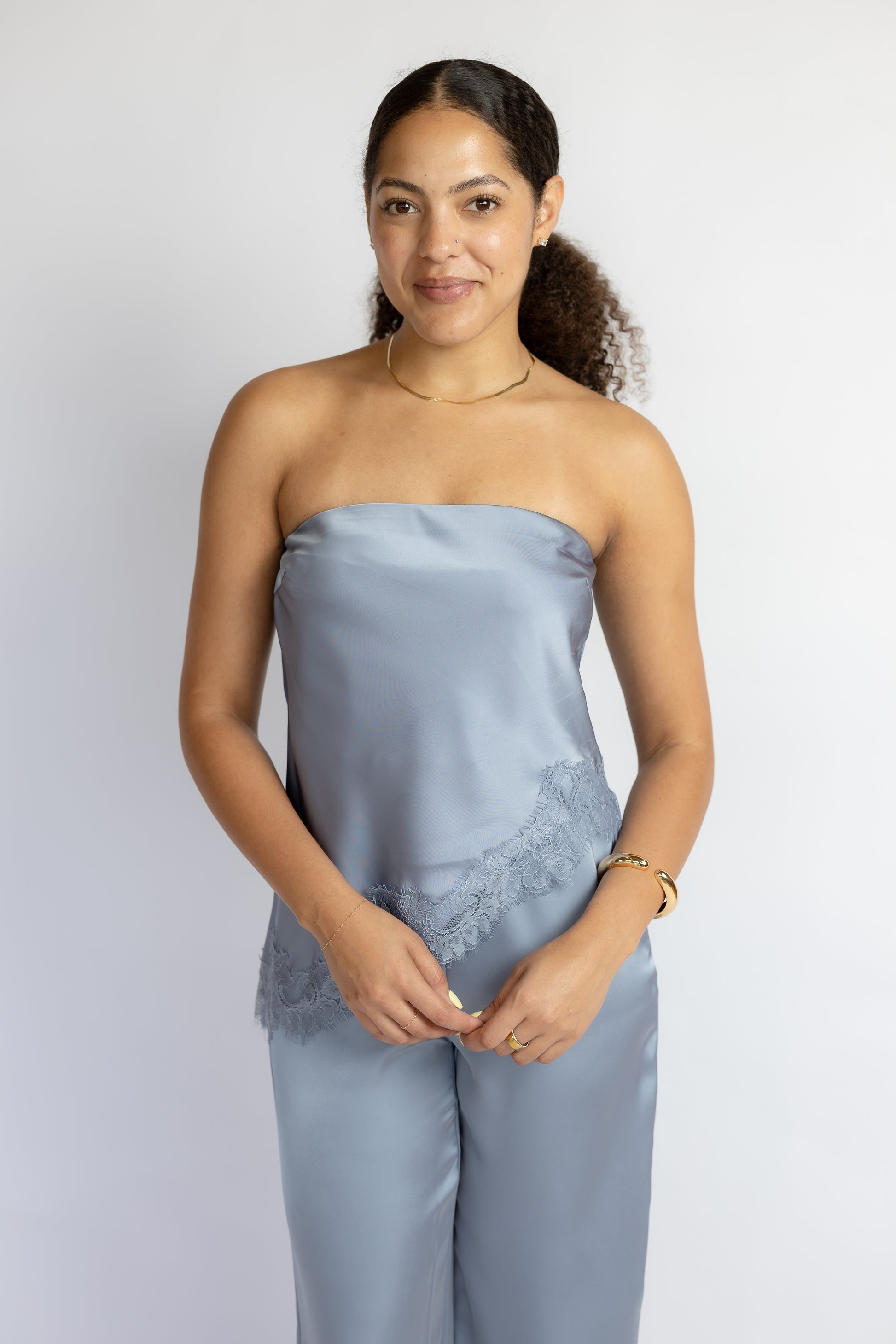 Woman wearing a light blue strapless top and pants with lace details on a white background