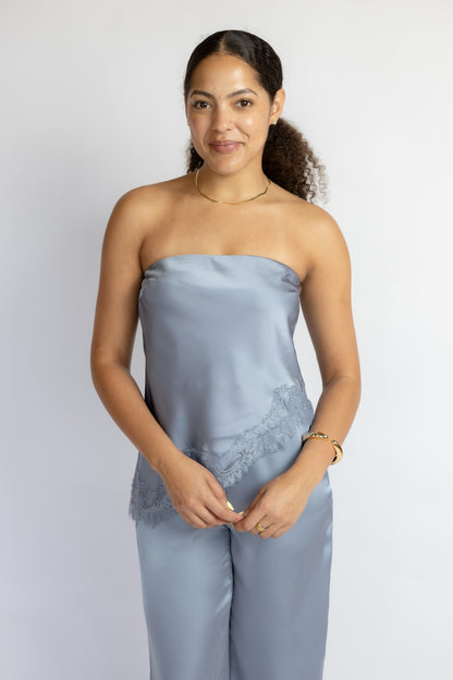 Woman wearing a light blue strapless top and pants with lace details on a white background