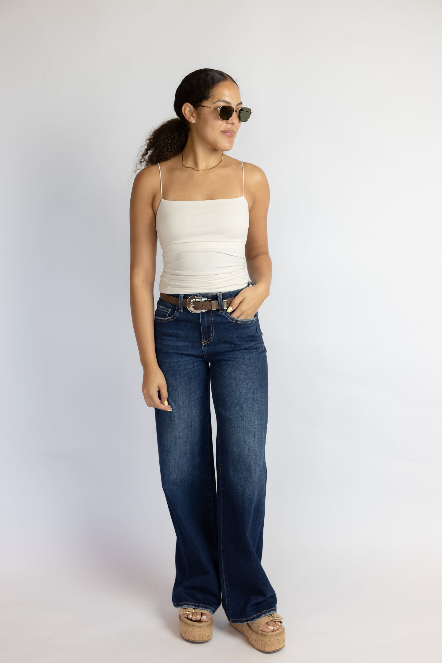 Woman wearing a white tank top and blue jeans against a plain background