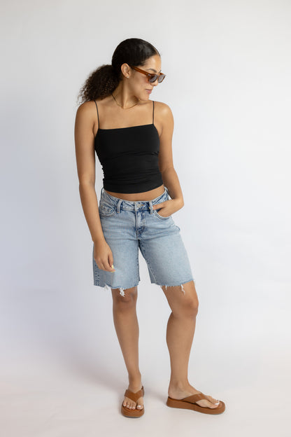 Woman wearing a black tank top and light blue denim shorts on a white background