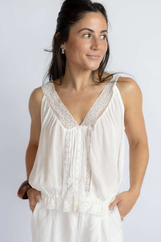 Woman wearing a white sleeveless top with lace details against a plain background