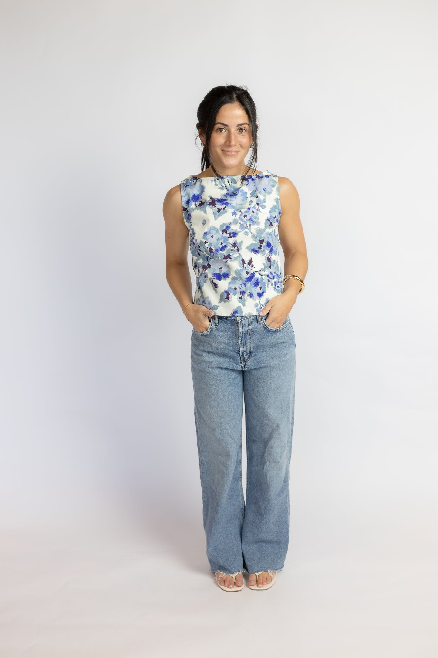 Woman wearing a sleeveless floral top and blue jeans on a white background