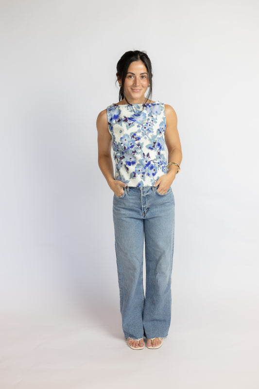 Woman wearing a sleeveless floral top and blue jeans on a white background