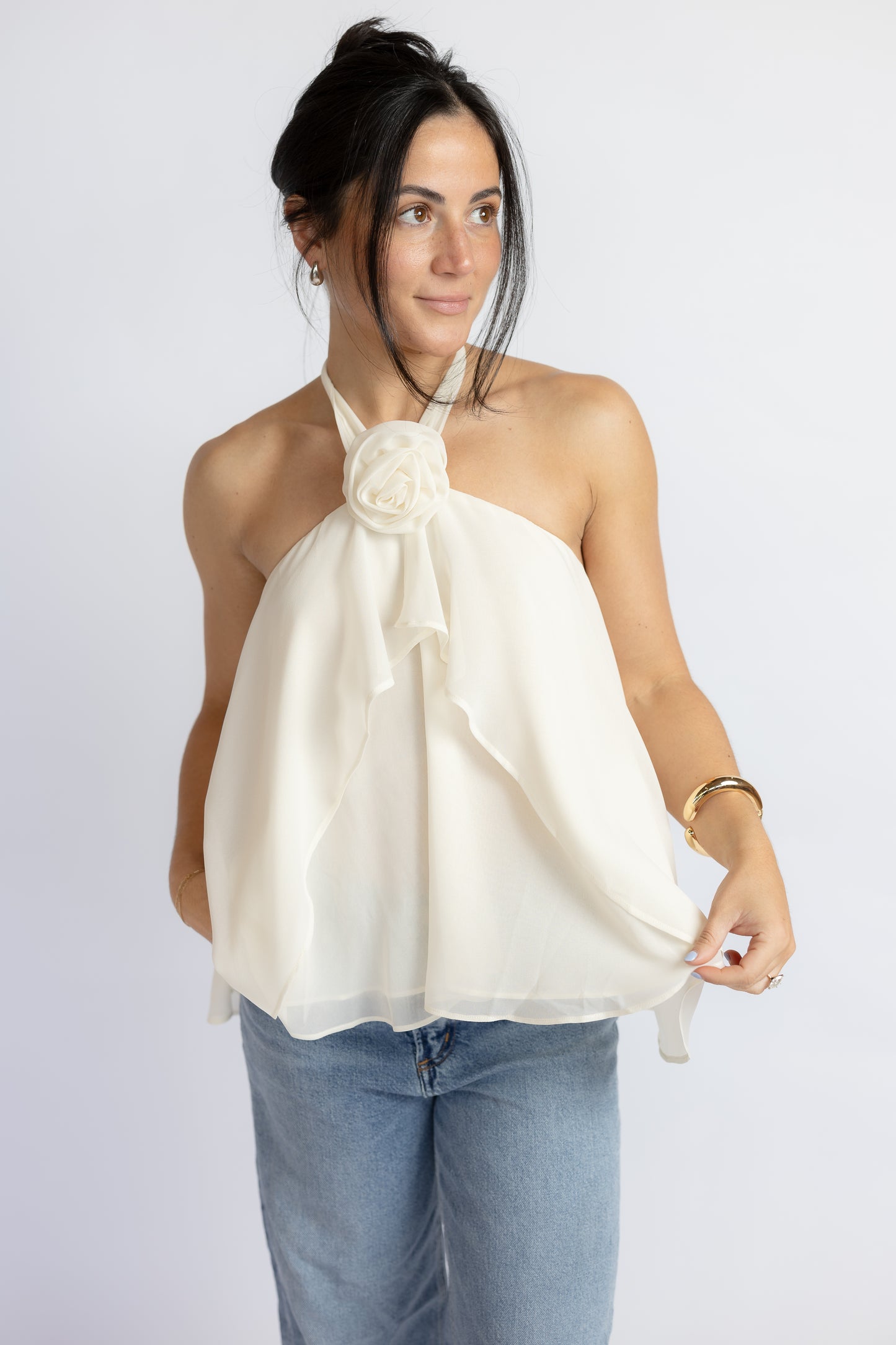 Woman wearing a white halter top with a floral detail against a plain background