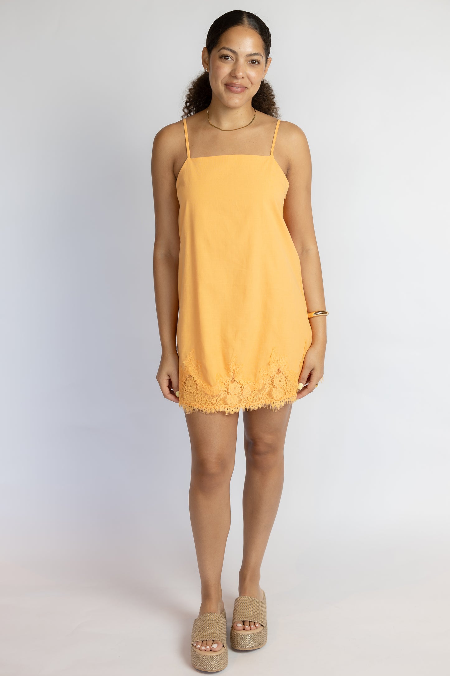 Woman wearing a bright orange lace dress against a white background