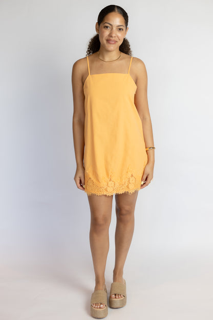 Woman wearing a bright orange lace dress against a white background