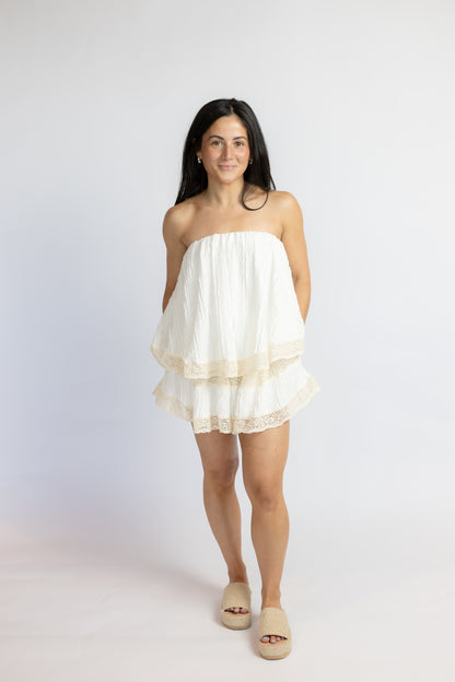 Woman wearing a white strapless romper on a plain background
