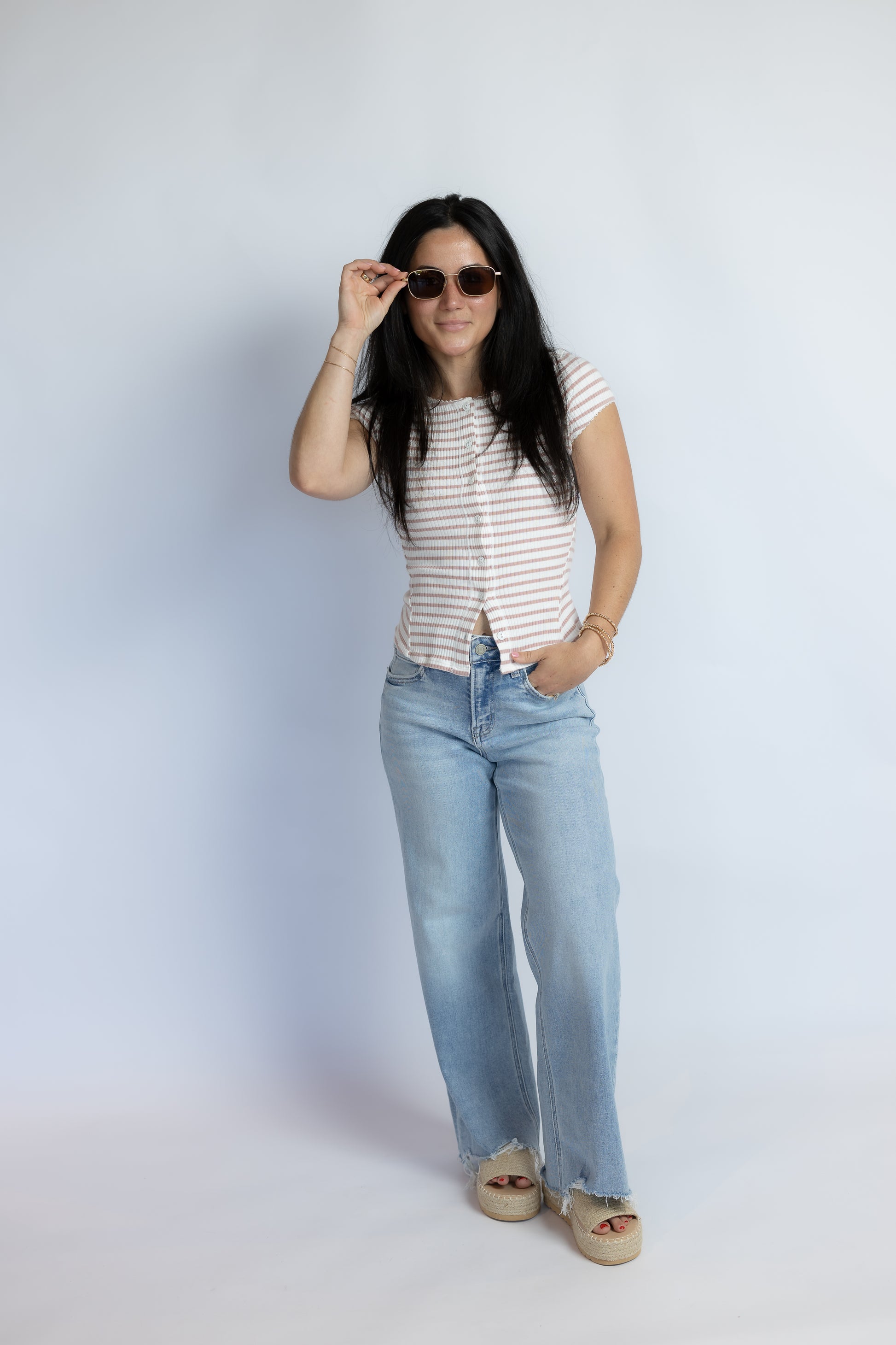 A woman modeling a short-sleeve striped top and light-wash wide-leg jeans against a plain light gray studio background.