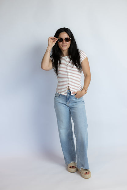 A woman modeling a short-sleeve striped top and light-wash wide-leg jeans against a plain light gray studio background.