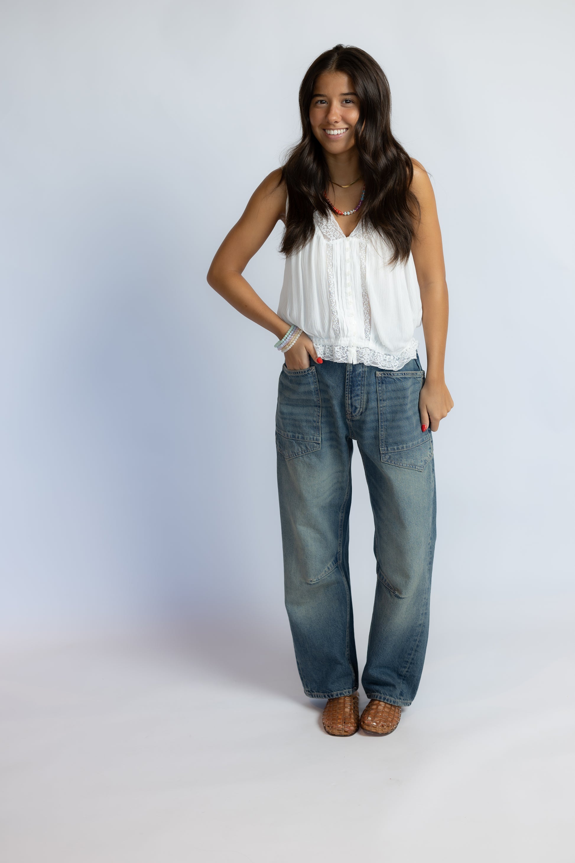 Model wearing Minimalist Moxie Boyfriend Jeans in size 25 with a white lace-trim tank and woven leather sandals