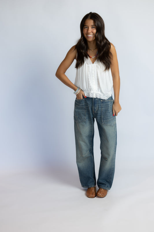 Model wearing Minimalist Moxie Boyfriend Jeans in size 25 with a white lace-trim tank and woven leather sandals