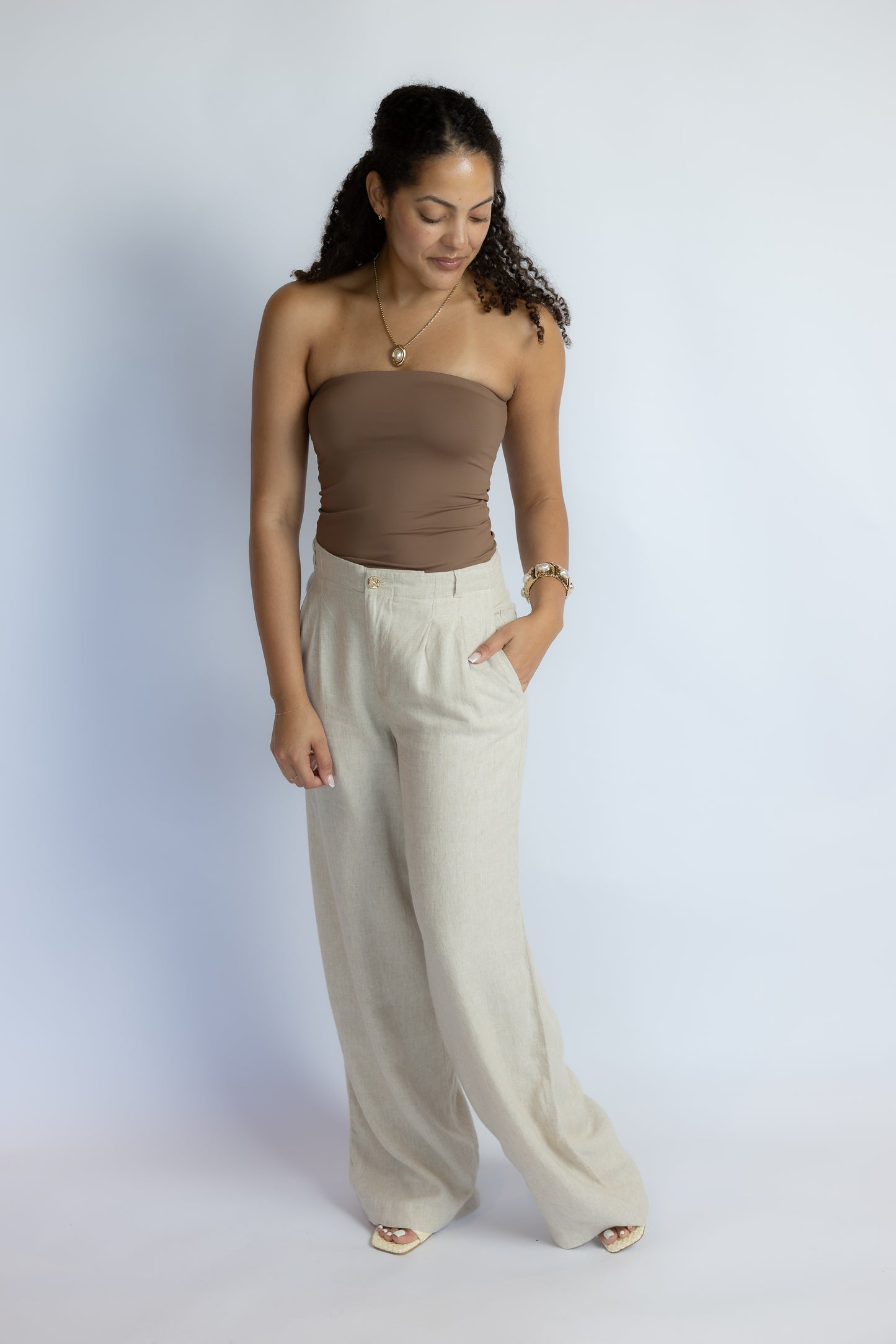 A woman modeling a brown strapless tube top and light beige wide-leg trousers against a light gray studio background.