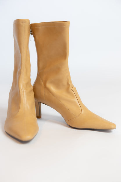 A pair of tan leather knee-high boots with pointed toes and mid-height stiletto heels, shown against a plain white studio background.