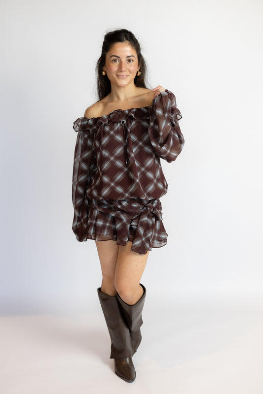 A woman modeling an off-the-shoulder plaid blouse and matching mini skirt set in dark brown and black, paired with dark brown knee-high boots, against a plain white studio background.
