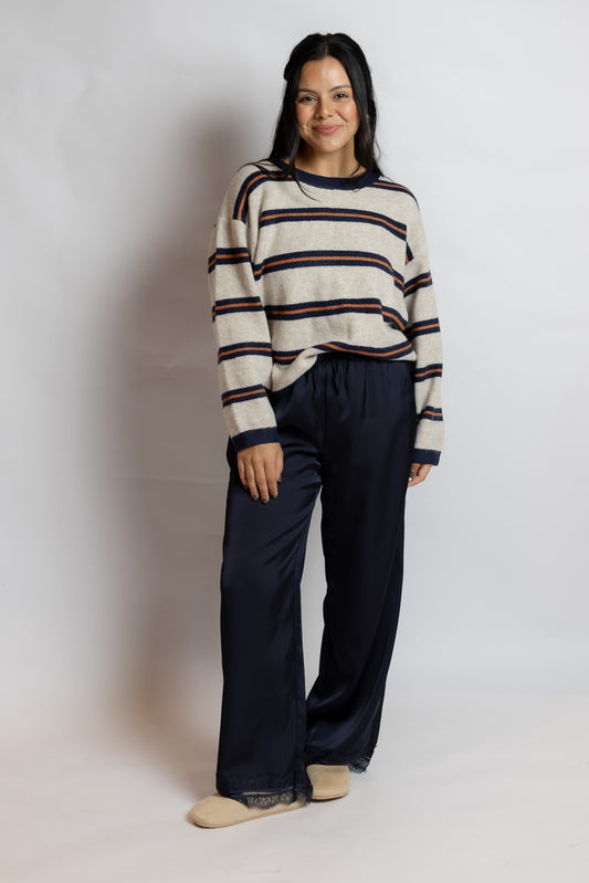 A woman modeling a striped knit sweater and dark navy wide-leg pants against a plain light gray studio background.