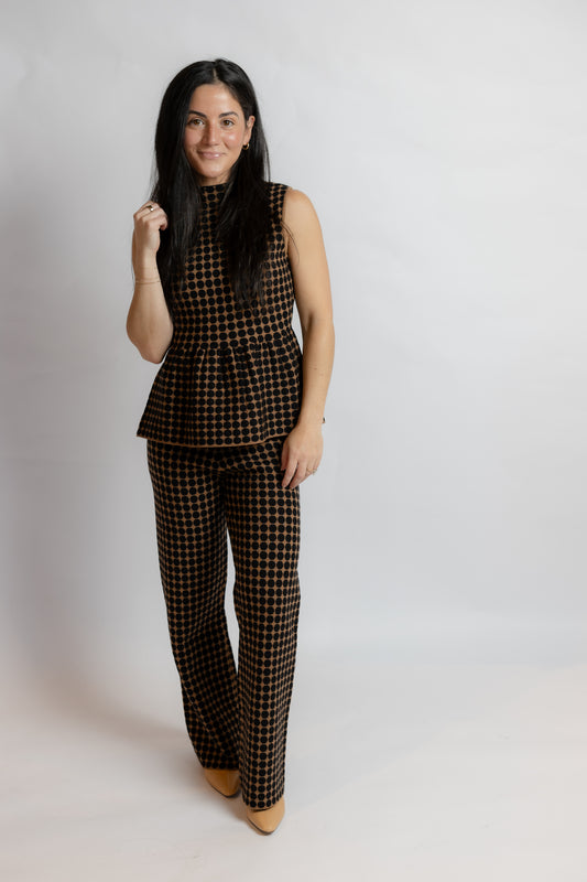 A woman modeling a matching sleeveless peplum top and wide-leg trousers set in a brown and black houndstooth pattern, standing against a plain light gray studio background.