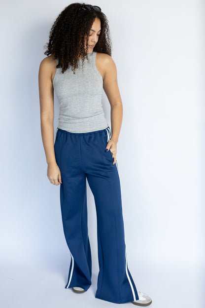 Woman wearing a gray sleeveless top and blue pants with white stripes on a white background