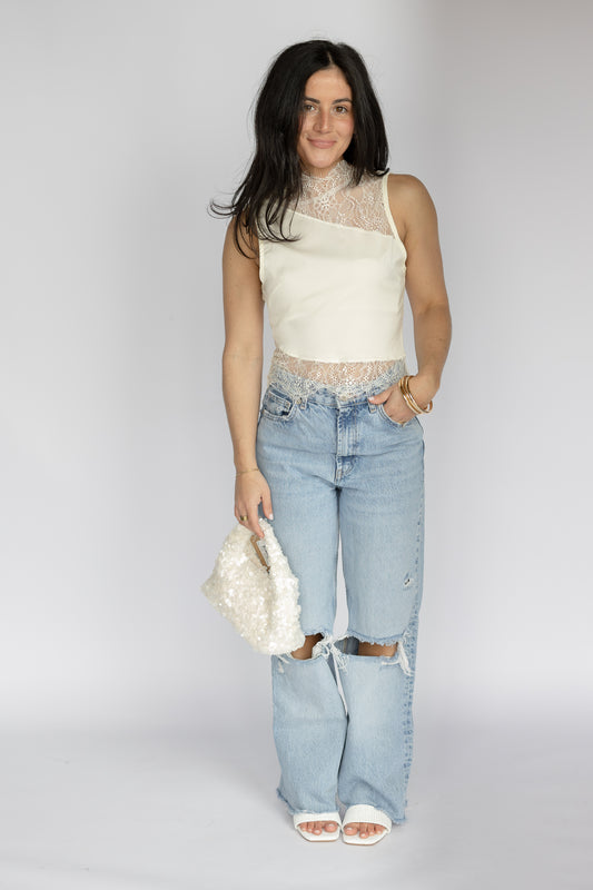 Woman wearing a white sleeveless top and light blue ripped jeans on a plain background