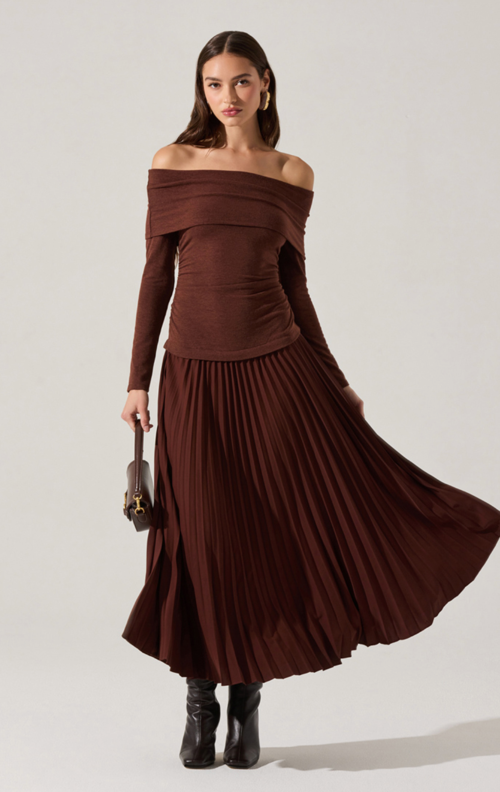 Model wearing the Tania Mixed Media Dress with off-shoulder neckline, ruched bodice, and pleated maxi skirt in chocolate brown
