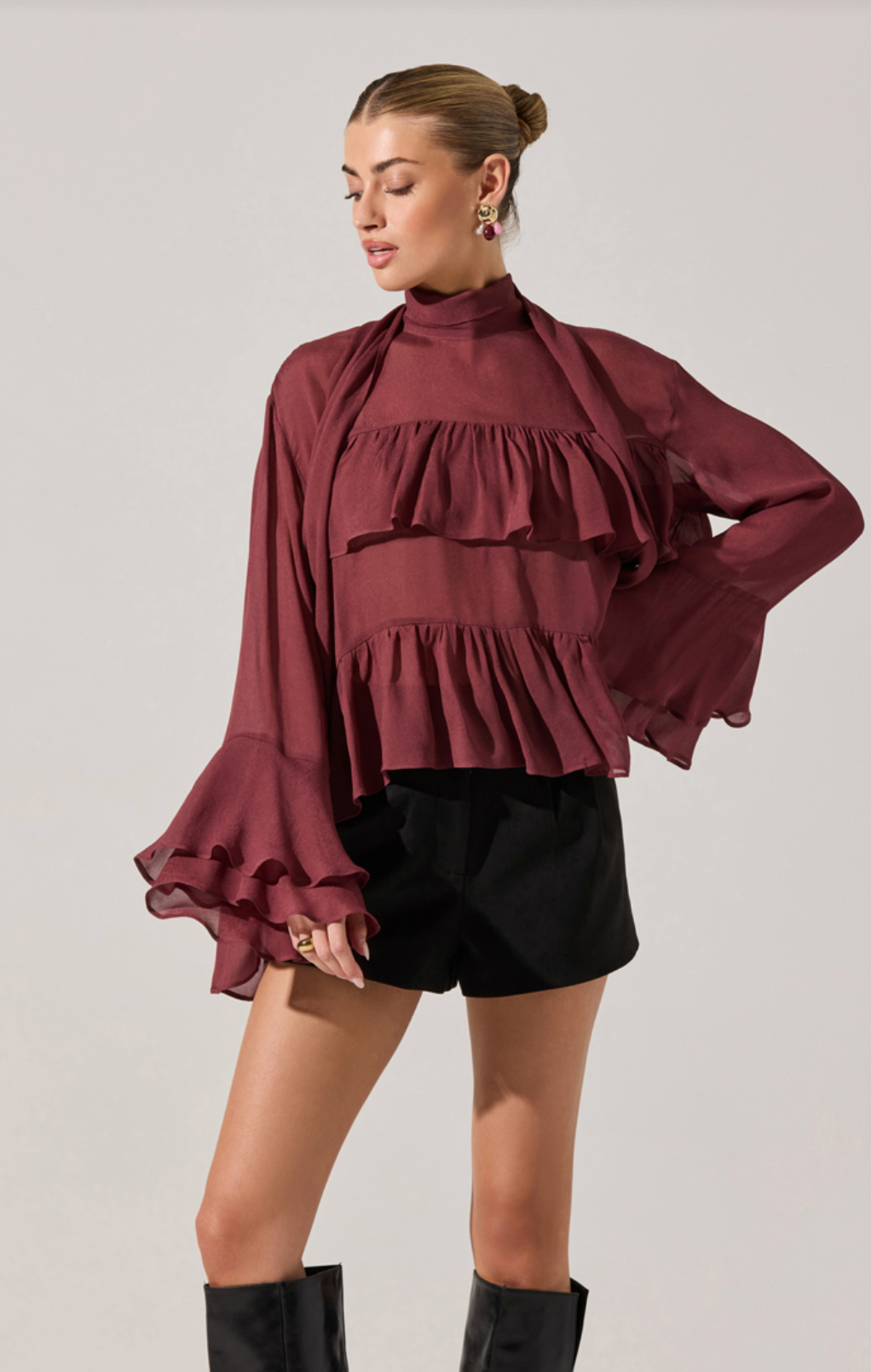 Model wearing the Fae Ruffle Top in burgundy chiffon with mock neck, scarf detail, and layered ruffles