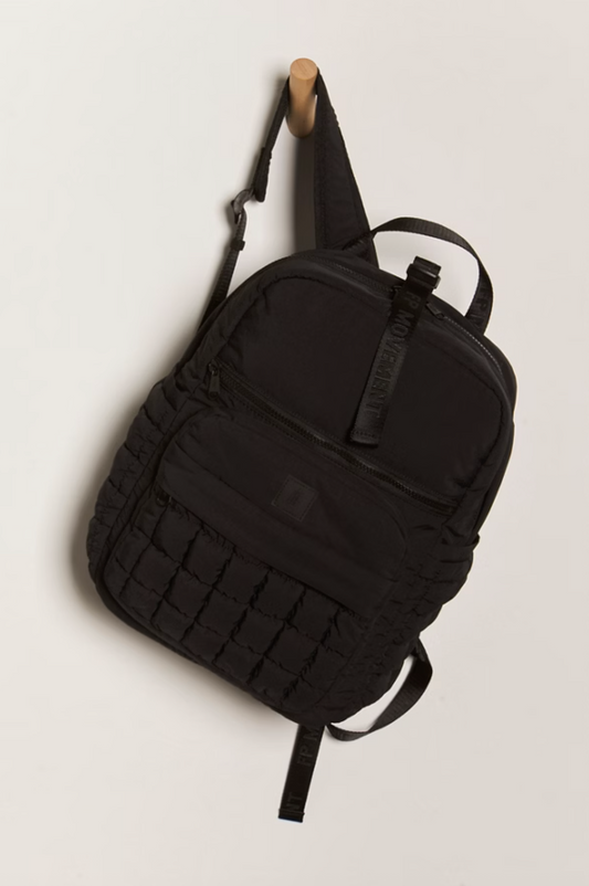 Model carrying Quilted Pack, black quilted backpack with front zip pocket and adjustable straps