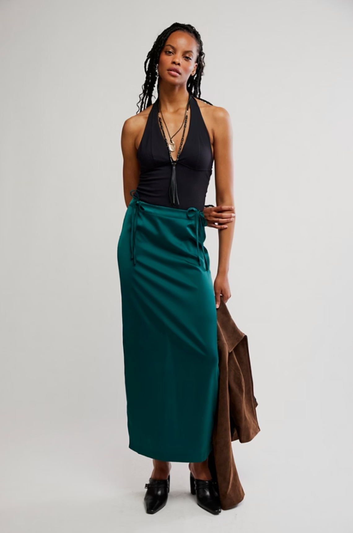 Model wearing satiny green column maxi skirt with bow tie details at hips and back slit.