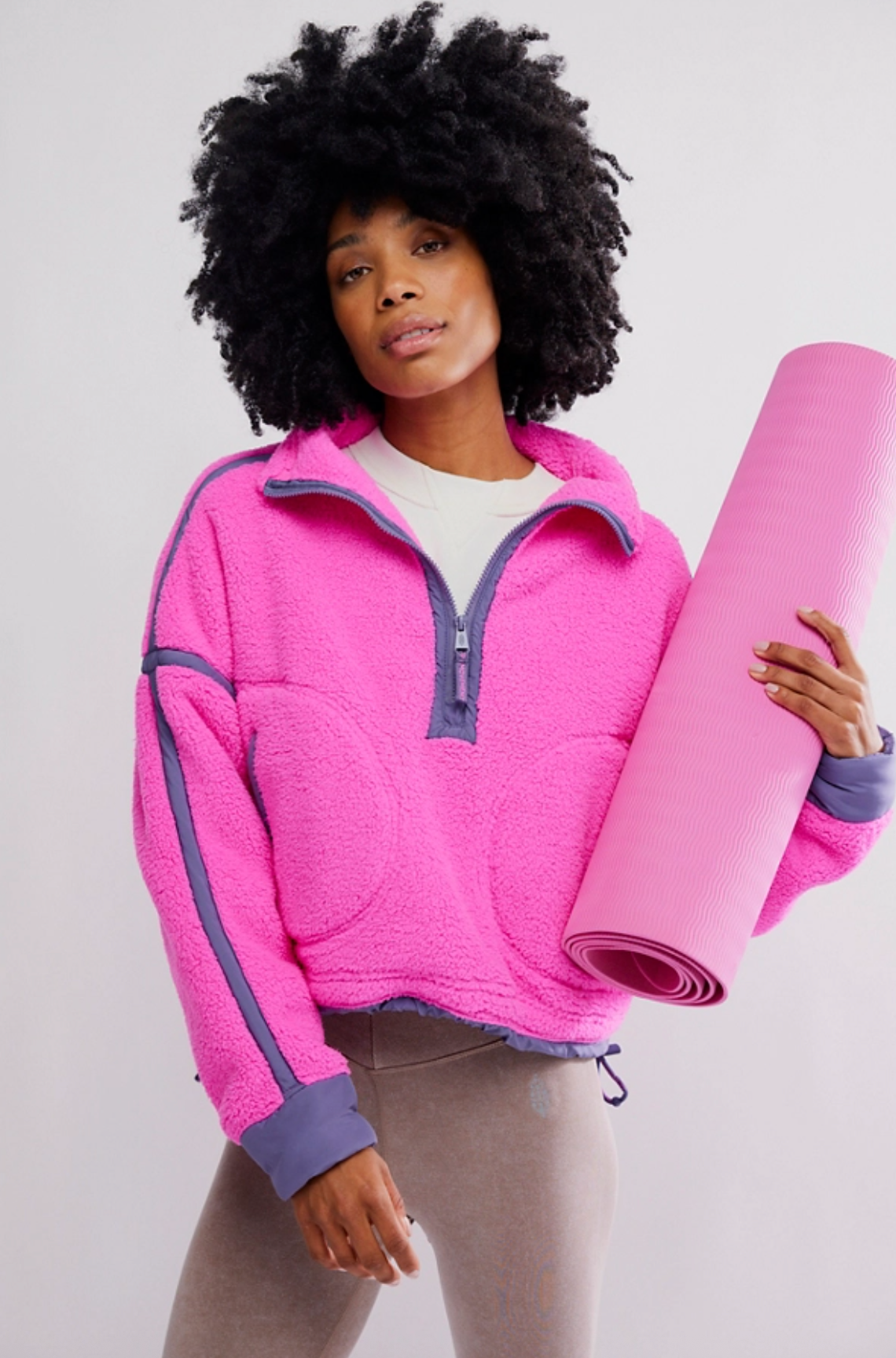 woman wearing pink fleece half-zip pullover with contrast seams holding a yoga mat