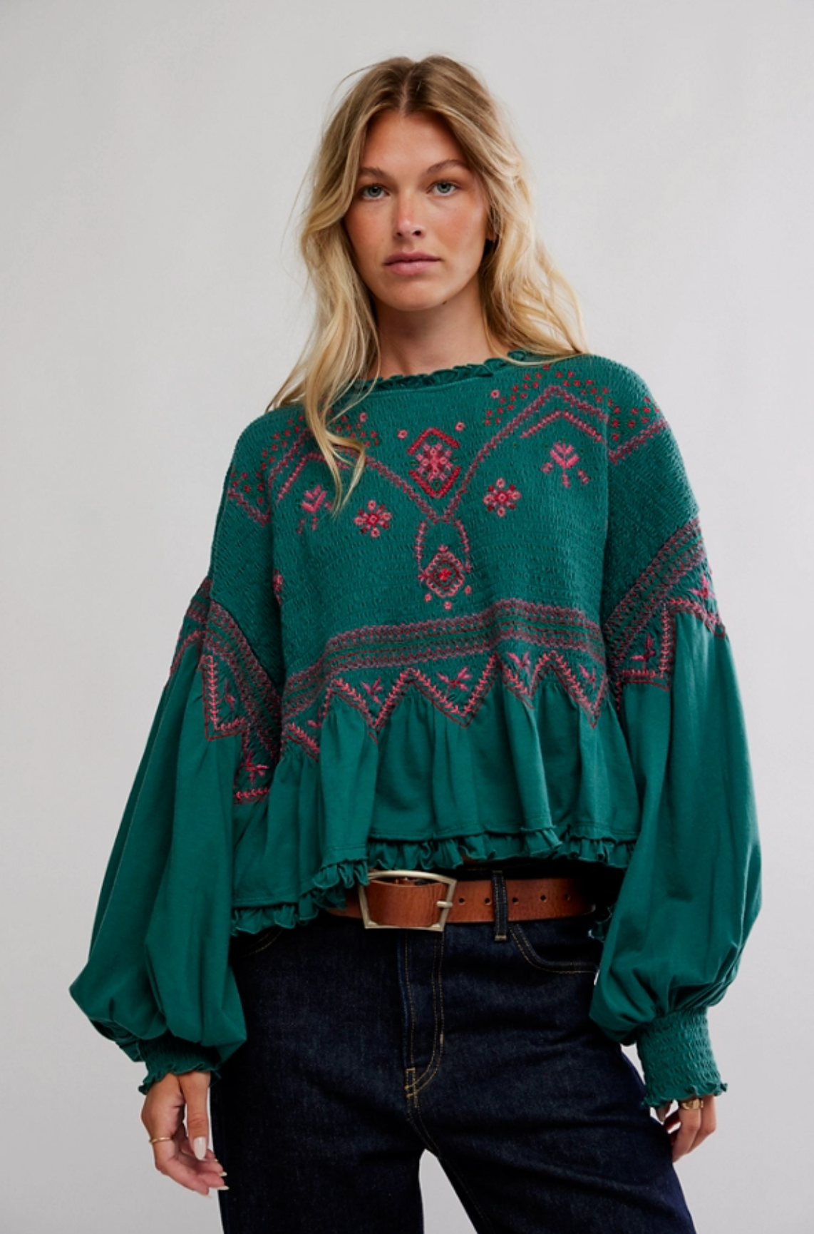 Woman wearing an emerald green embroidered peplum top with long balloon sleeves and ruffled trim.