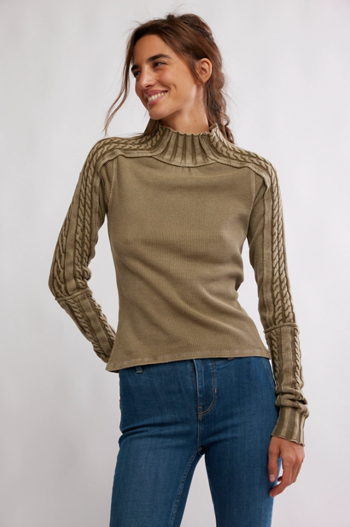 Woman wearing an olive waffle knit sweater with cable-knit sleeve details and mock neckline styled with blue denim jeans.
