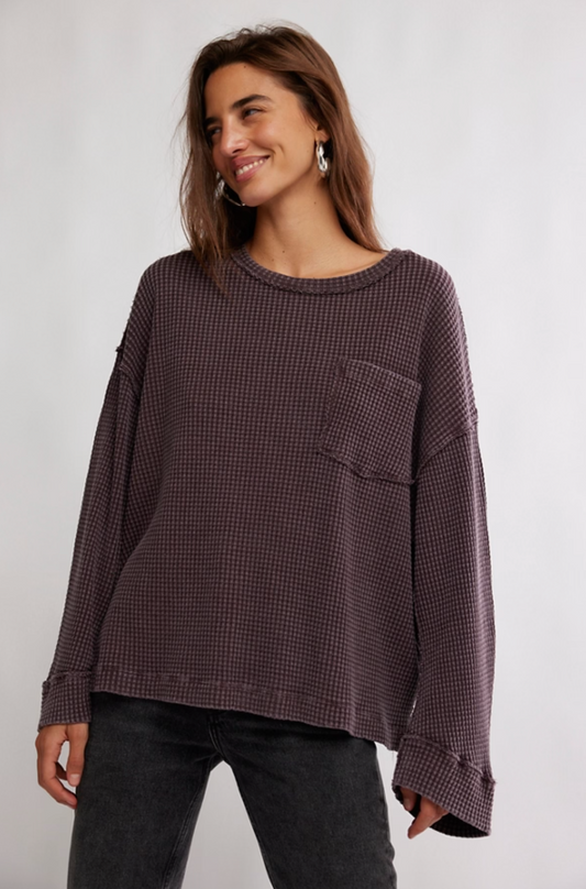 Woman wearing a dark waffle knit oversized long sleeve top with drop shoulders and front patch pocket styled with black jeans.