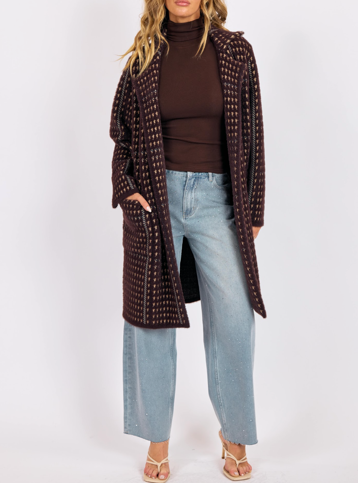 Woman wearing a chocolate brown houndstooth knit coat layered over a brown turtleneck and light denim jeans.