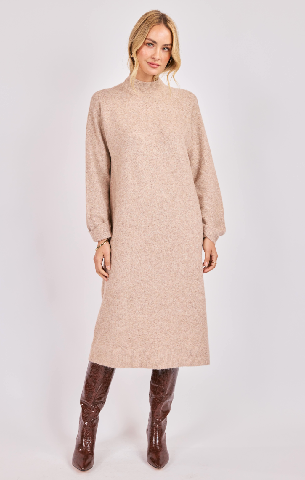 Woman wearing a beige knit turtleneck midi dress with long sleeves and brown knee-high boots.