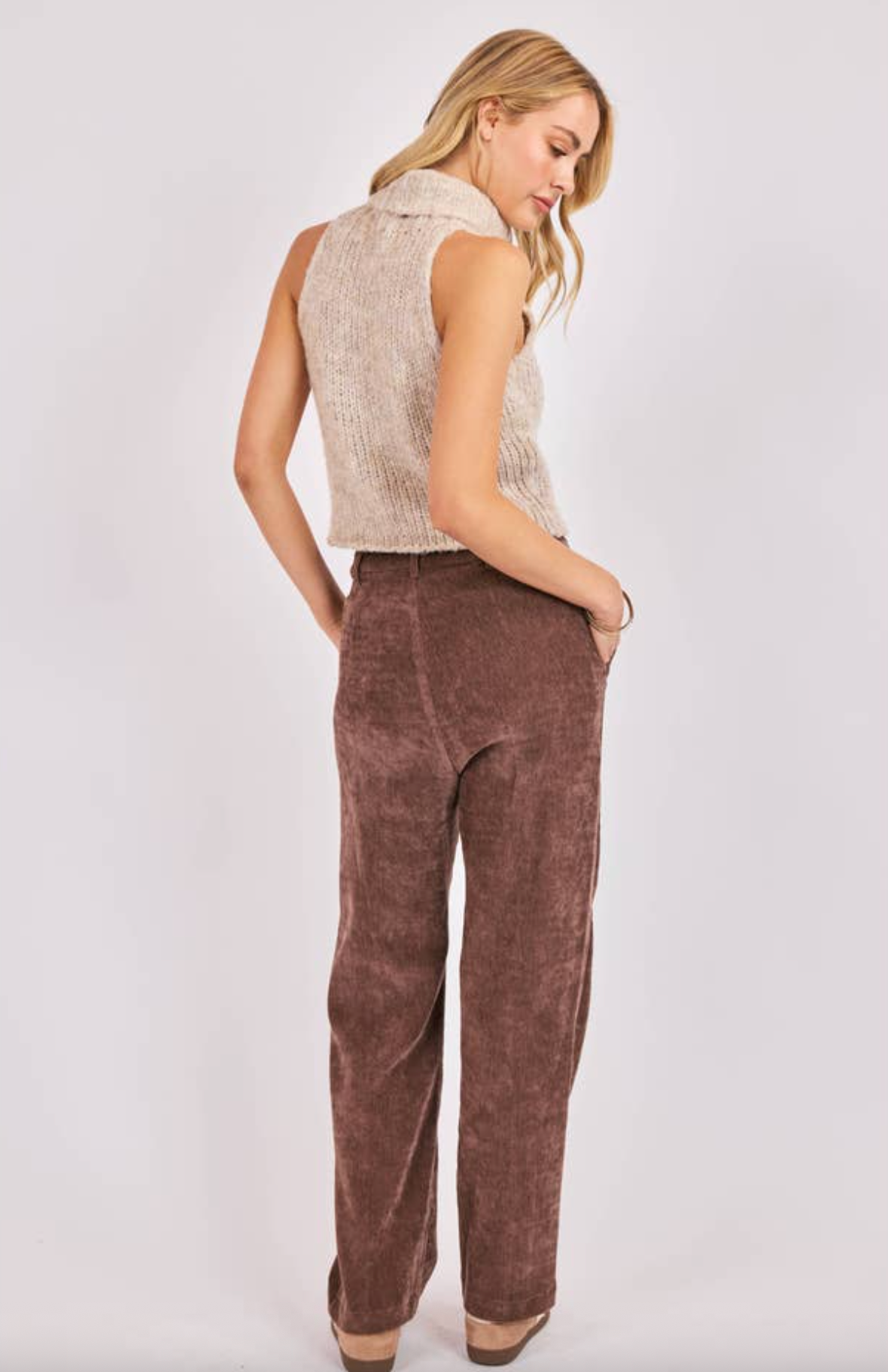 Woman wearing a sleeveless beige top and brown corduroy pants on a white background